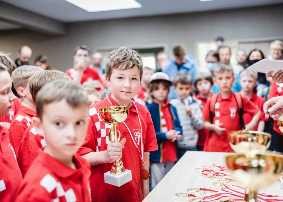 Chłopiec w czerwonej koszulce trzyma puchar wśród dzieci, Akademia Szachowa Gliwice