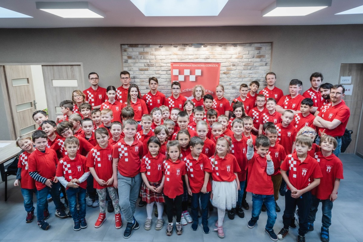 Duża grupa dzieci i trenerów w czerwonych koszulkach pozuje do zdjęcia, Akademia Szachowa Gliwice