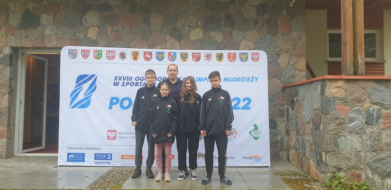 Grupa młodzieży pozuje przed banerem olimpiady młodzieży w sporcie, Fundacja Jaćwież z Suwałk