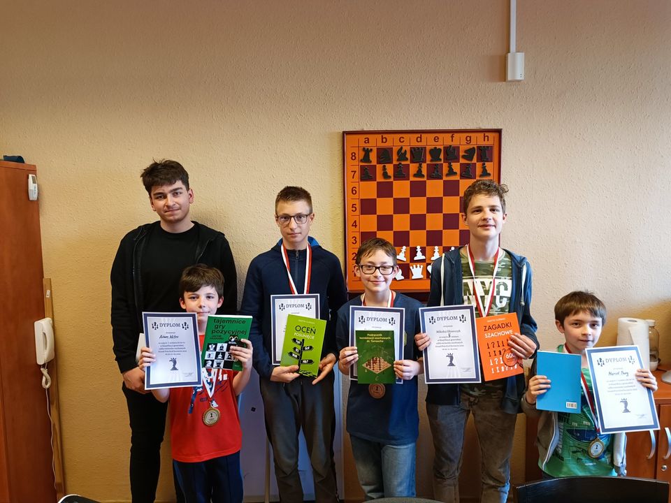 Dzieci z medalami i dyplomami pozują przed tablicą demonstracyjną, klub szachowy KSz Gryf Szczecin