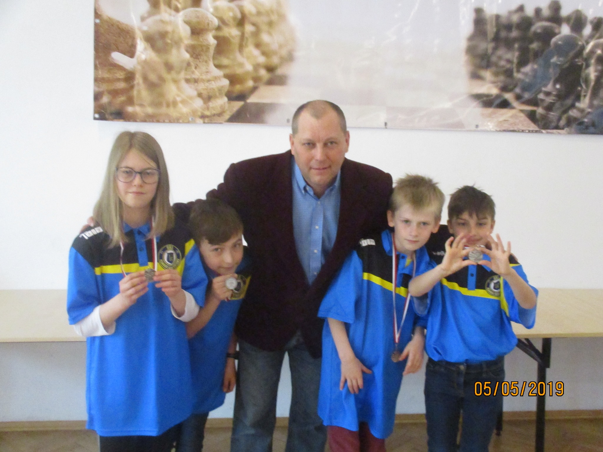 Dzieci w niebieskich koszulkach z medalami pozują z trenerem, UKS Pijarski KS z Łowicza