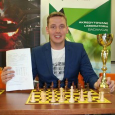 Mężczyzna w garniturze trzyma puchar przy szachownicy, trener szachów Tomasz Warakomski z Gliwic