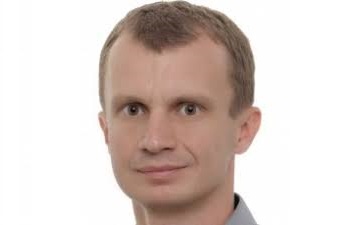 Mężczyzna w garniturze pozuje do zdjęcia portretowego, trener szachów Piotr Szymański z Warszawy