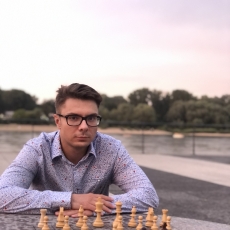 Mężczyzna w okularach siedzi przy szachownicy z figurami na tarasie, trener szachów Władysław Żelak z Warszawy