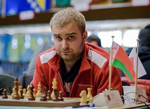 Mężczyzna w czerwonej bluzie siedzi przy szachownicy na turnieju, trener szachów Marcin Tazbir z Piotrkowa Trybunalskiego