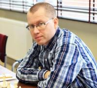 Mężczyzna w kraciastej koszuli siedzi przy szachownicy, trener szachów Dariusz Baumann z Bydgoszczy