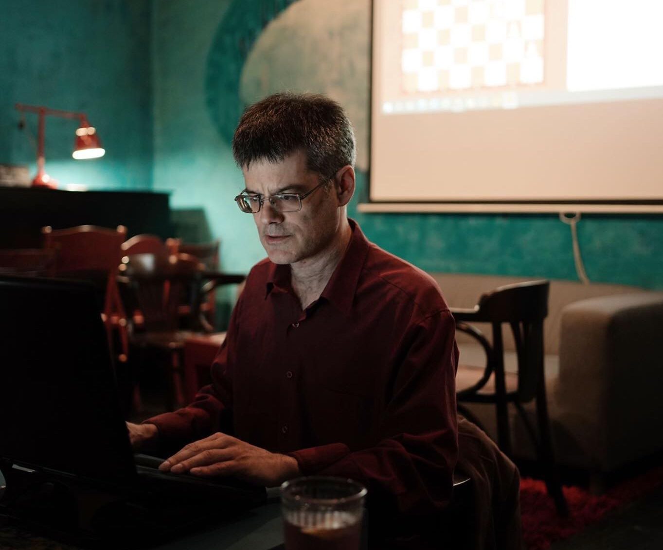 Mężczyzna pracuje przy laptopie, w tle ekran z diagramem szachowym, trener szachów Piotr Kaim z Krakowa