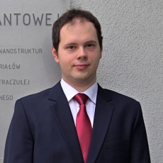 Mężczyzna w garniturze i krawacie stoi przed ścianą z napisami, trener szachów Konrad Drozdowski z Torunia