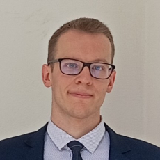 Mężczyzna w okularach i garniturze pozuje na jasnym tle, trener szachów Tomasz Jankowiak z Wrocławia