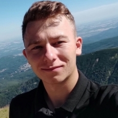 Mężczyzna w czarnej koszulce na tle górskiego krajobrazu, trener szachów Tomasz Nowak z Poznania