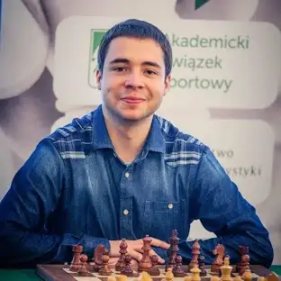 Mężczyzna w dżinsowej koszuli siedzi za szachownicą z figurami, trener szachów Maciej Klekowski z Krakowa