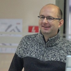Mężczyzna w swetrze uśmiecha się we wnętrzu budynku, trener szachów Łukasz Cyborowski z Legnicy